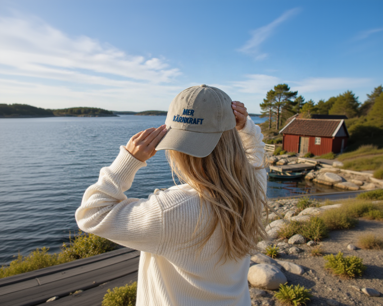 Person som bär beige Mer kärnkraft-keps med blå brodyr vid vattnet.